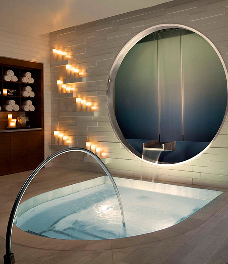 Indoor hydrotherapy plunge with cascade jet and candlelit stone wall, wellness spa concept rendering by Aquatics International Group
