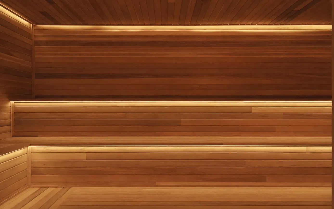 Finished custom cedar sauna interior with tiered benches and continuous LED strip lighting under each bench and at the ceiling line