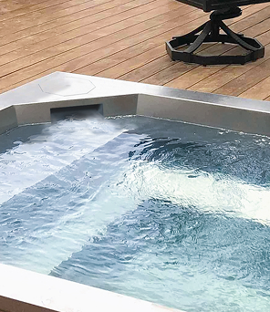 Brushed stainless steel spa set into a wood deck, stainless steel pool and spa vessels by Aquatics International Group
