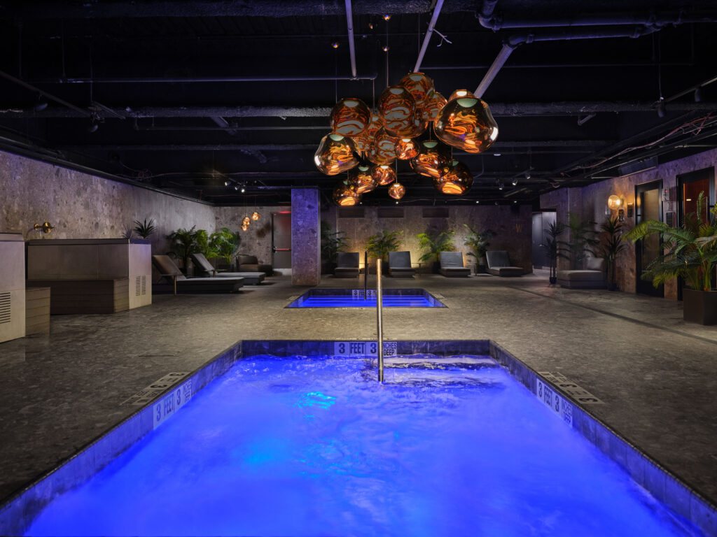 Indoor plunge pool with blue LED lighting under a copper pendant chandelier, TMPL NYC aquatic wellness facility by Aquatics International Group